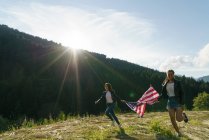 Zwei gut gelaunte Frauen laufen mit Fahne auf die Natur zu — Stockfoto
