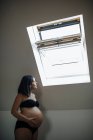 Pregnant looking upwards at garret openned window. Side view. — Stock Photo
