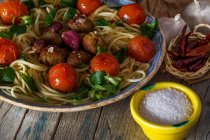 Close up view of plate with italian pasta with meatballs cherry tomatoes served with salt and peppers in small bowls — Stock Photo