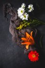 Patrón floral creativo con varias flores coloridas y tela de la mirada en la superficie oscura - foto de stock
