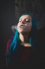 Portrait of blue haired girl posing at camera and smoking out cigarette smoke — Stock Photo
