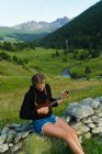 Mulher sentada na cerca de pedra rural na natureza e jogando ukulele — Fotografia de Stock