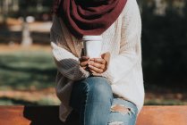 Mittelteil-Ansicht einer Frau, die im Park auf einer Bank sitzt und eine Tasse Kaffee in der Hand hält — Stockfoto