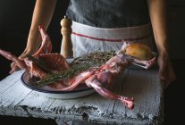 Close-up of woman holding carcass of raw rabbit with ingredients on wooden table — Stock Photo