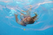 Child swimming in pool with turquoise water and looking at camera — Stock Photo