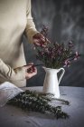 Immagine ritagliata di fiorista femminile che taglia con forbici bouquet di fiori in vaso bianco — Foto stock