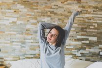 Girl sitting in bed and stretching — Stock Photo