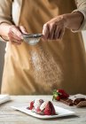 Metà sezione di femminile versando zucchero a velo con colino sul piatto con dolce di fragole fresche — Foto stock