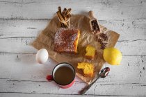 Sopra vista di fette di torta al limone su carta da forno con ingredienti su tavolo rustico — Foto stock