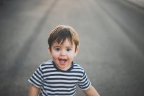 Porträt eines überraschten kleinen Jungen, der mit offenem Mund auf Asphaltstraße in die Kamera blickt — Stockfoto