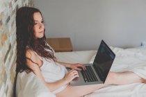 Mujer relajante en la cama y el uso de ordenador portátil - foto de stock