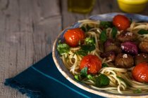 Crop image of plate of pasta with meatballs and cherry tomatoes on towel over rustic wooden table — Stock Photo