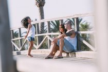 Eltern sitzen am Geländer und betrachten springende Tochter — Stockfoto
