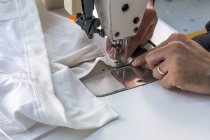 Manos de los cultivos de costura en la maquinaria de tela blanca - foto de stock