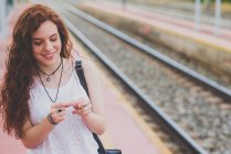 Портрет девушки с веснушками и ветреными рыжими волосами, закуривающей сигарету на железнодорожной платформе — стоковое фото