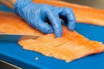 Mano maschile in guanti sta tagliando il salmone a fette . — Foto stock