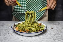 Close up view of female hands winding on fork italian green tagliatelle — Stock Photo