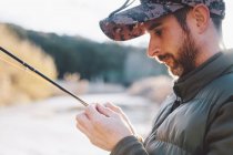 Portrait of mature man preparing hook for fishing at river — Stock Photo