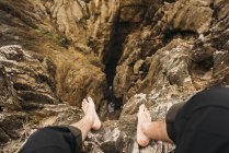 Mirando hacia abajo vista de los pies desnudos sobre acantilados rocosos - foto de stock