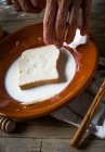 Close-up vista de mão colocando fatia de pão na placa com leite — Fotografia de Stock