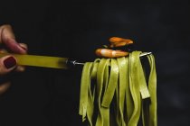 Green tagliatelle with seafood on fork on black background — Stock Photo