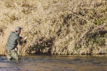 Visão traseira da pesca do pescador com haste na costa do rio — Fotografia de Stock
