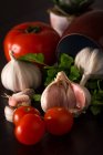 Dientes de ajo fresco con tomates frescos y perejil sobre fondo oscuro con frasco - foto de stock