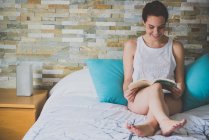 Дівчина сидить на ліжку і читає книгу — стокове фото