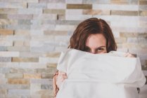 Mädchen versteckt Gesicht mit Kissen und blickt in Kamera — Stockfoto