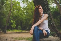 Portrait à angle bas de fille avec de longs cheveux roux bouclés assis sur la pierre dans les bois et regardant de côté — Photo de stock