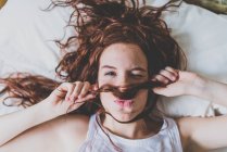 Жінка лежить в ліжку, використовуючи волосся як вуса — стокове фото
