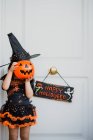 Menina em traje de bruxa escondendo rosto com saco de abóbora — Fotografia de Stock