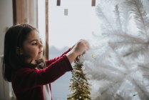 Seitenansicht eines lächelnden Mädchens, das Christbaumkugeln auf den dekorativen Weihnachtsbaum legt — Stockfoto