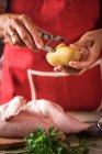 Gros plan des mains féminines épluchant les pommes de terre crues pour rôtir avec du poulet — Photo de stock