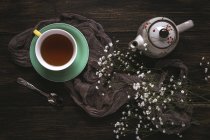 Cup of tea and teapot with wildflowers on brown surface — Stock Photo