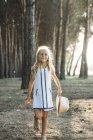 Charmantes kleines Mädchen posiert mit Hut im sonnenbeschienenen Wald — Stockfoto