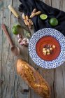 Sopa de tomate em prato estampado em mesa de madeira com pão e ingredientes — Fotografia de Stock