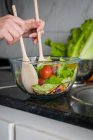 Abgeschnittenes Bild von Händen, die Salat in Schüssel am Küchentisch mischen — Stockfoto