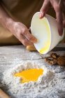 Immagine di raccolto di mani che aggiungono uova schiacciate in pila di farina su tavolo rustico di legno — Foto stock