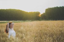 Портрет молодої рудої волохатої дівчини в білій сукні дивиться на камеру і позує на житнє поле — стокове фото