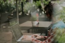 Вид збоку бородатий чоловік сидить за столом тераси кафе і використовує ноутбук — стокове фото