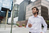 Ritratto di uomo d'affari bruna che tiene lo smartphone in mano e distoglie lo sguardo sulla scena urbana del centro — Foto stock