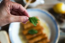 Crop hand holding mint leaves over plate with dessert — Stock Photo