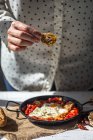 Крупним планом вид руки тримає копійки з жовтком над сковородою з яєць і сушених помідорів — стокове фото