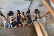 Vista ad alto angolo di due donne allegre con borse in piedi sulla scala mobile — Foto stock