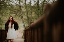 Спокойная рыжая девушка позирует на деревянном мосту в сельской местности — стоковое фото