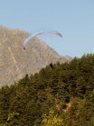 Distant view of person paragliding over forest covered mountains — Stock Photo