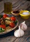 Imagen de la cosecha de plato lleno de pasta con albahaca y tomates cherry en la mesa de madera rústica con ajo y platos con especias - foto de stock