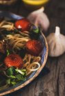 Crop image of plate full of pasta with basil and cherry tomatoes on rustic wooden table with garlic — Stock Photo