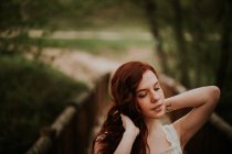 Sensual ginger girl with tattoo on wrist adjusting hair at nature — Stock Photo